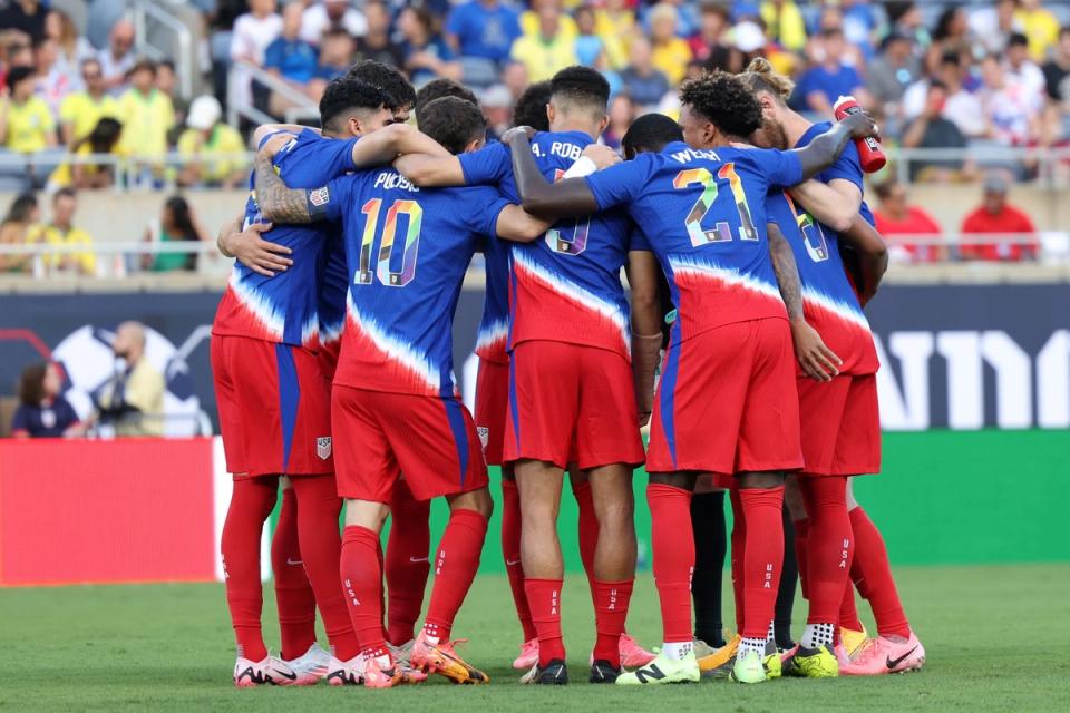 usmnt players huddle up midfield with blue and red kits on during a match against brazil