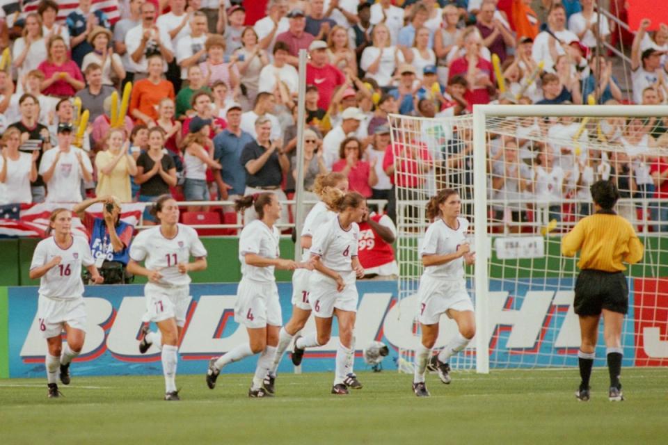 Six USWNT players run onto the pitch from behind the goal during a 1999 Women's World Cup match against Germany