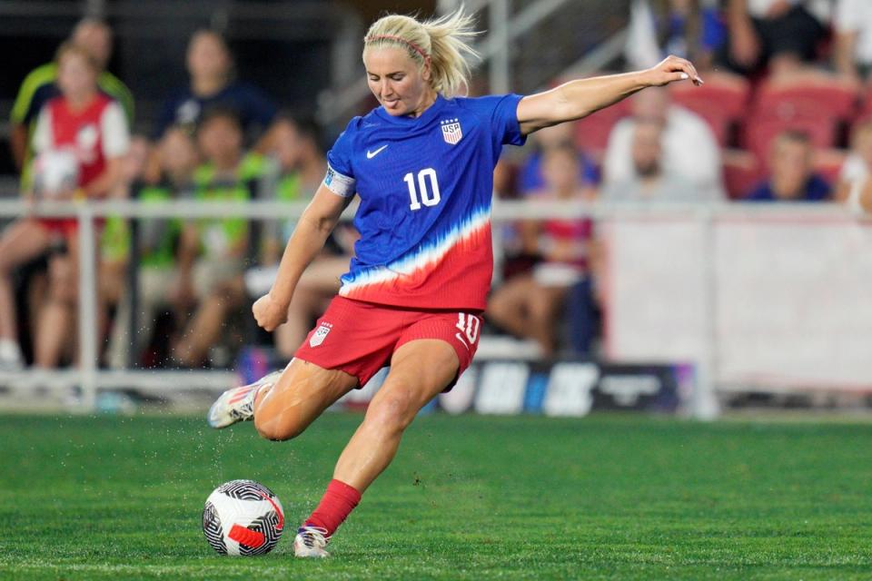 Lindsey Horan looks down at a ball as she prepares to kick it during a match in a blue and red kit and red shorts