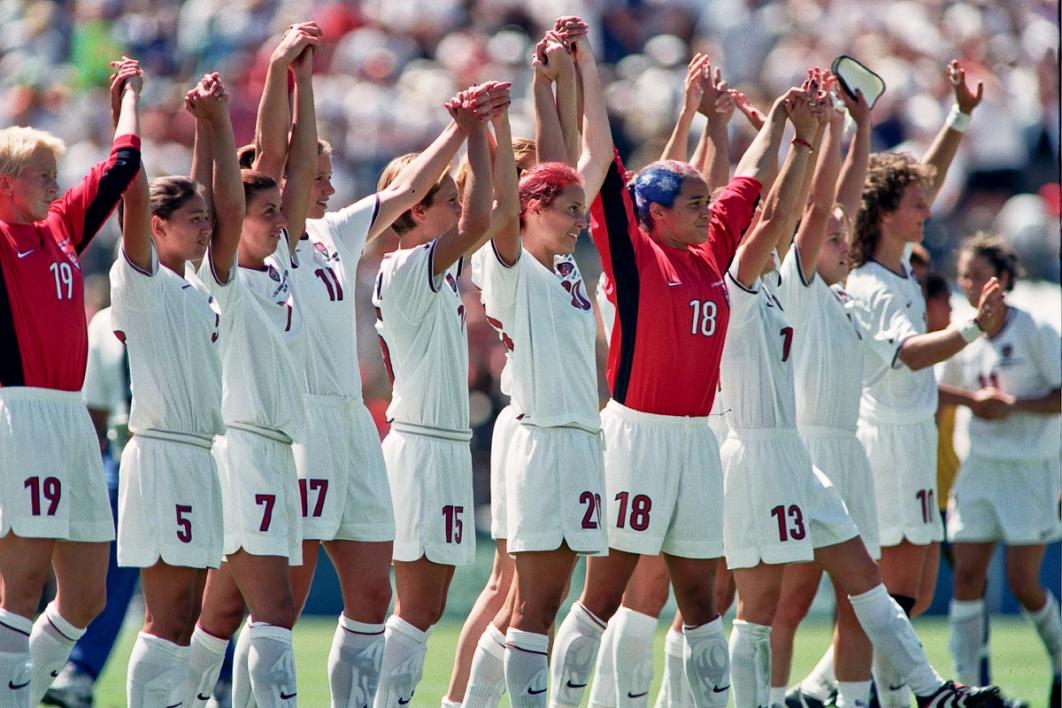 1999 USWNT players linking hands and waving to the crowd
