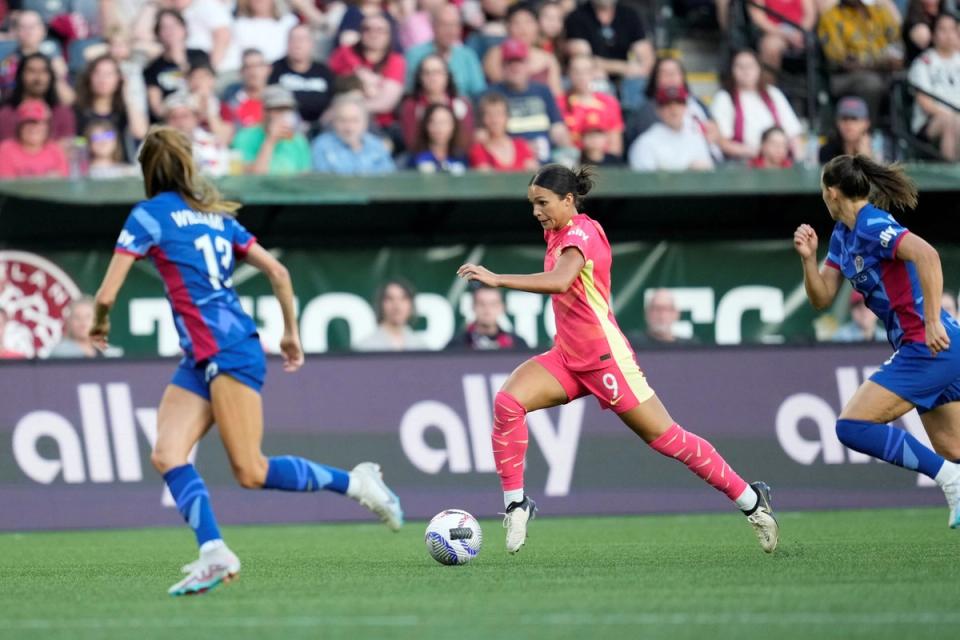 sophia smith dribbles the ball in a red thorns kit with two defenders closing in
