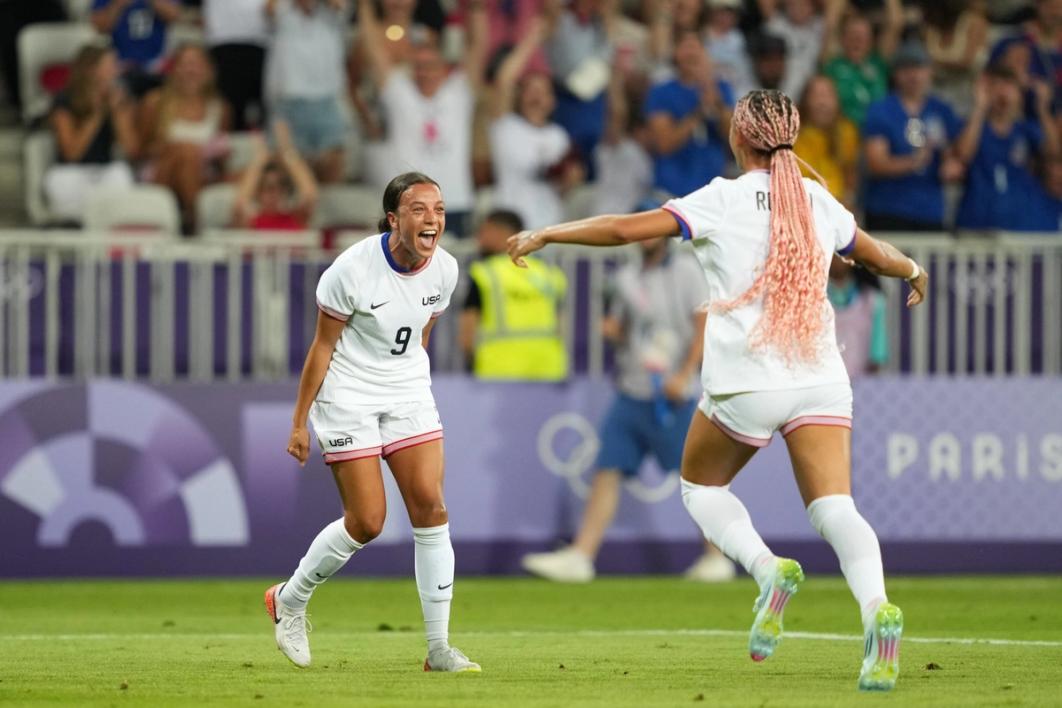 Mallory Swanson and Trinity Rodman in white jersey and shorts celebrate a goal on the field during the match against Zambia