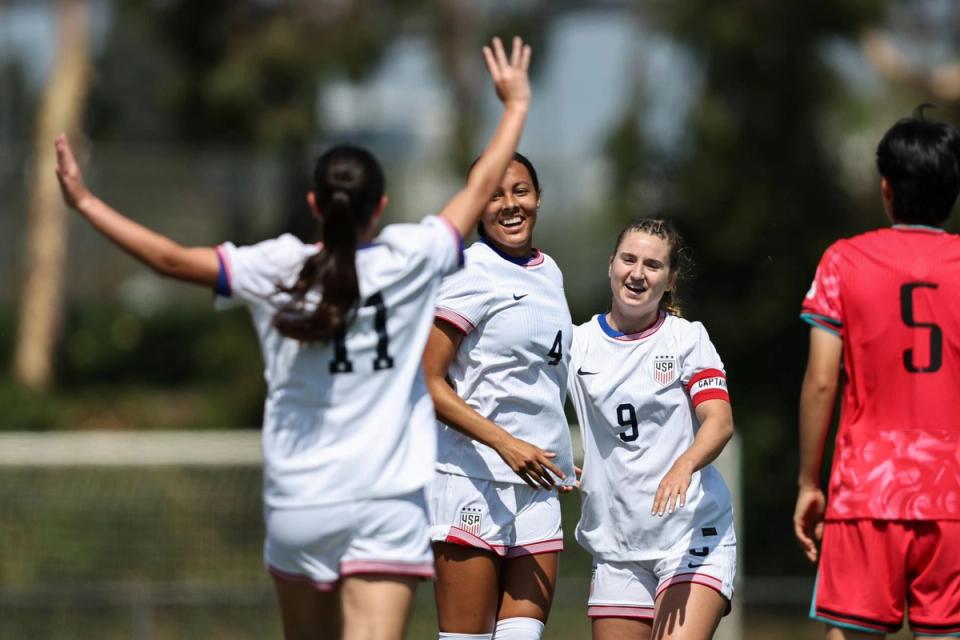 three u 20 players celebrate on field in white jersey white shorts