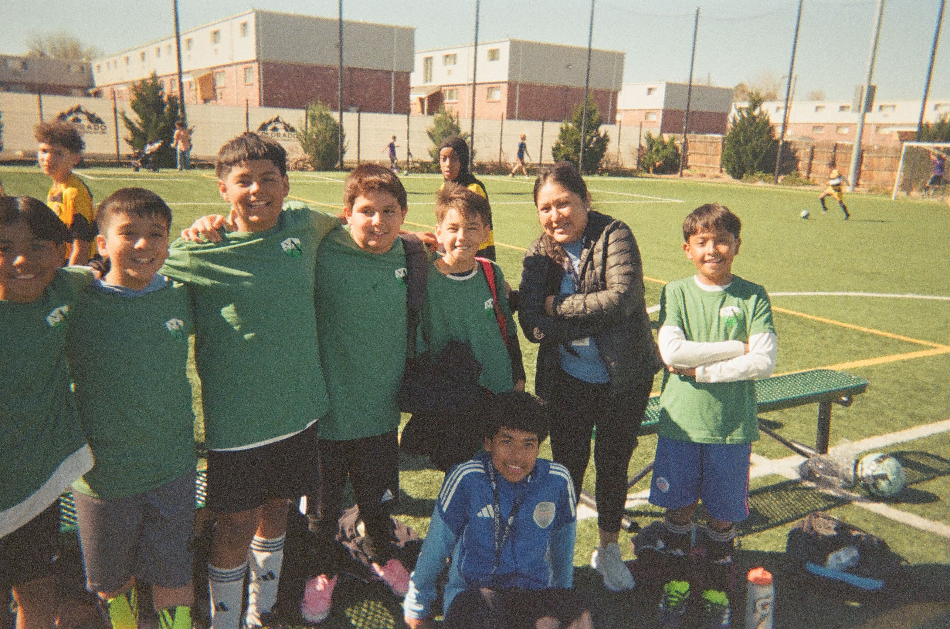 Group of young soccer players posing together on the sidelines during a match day.