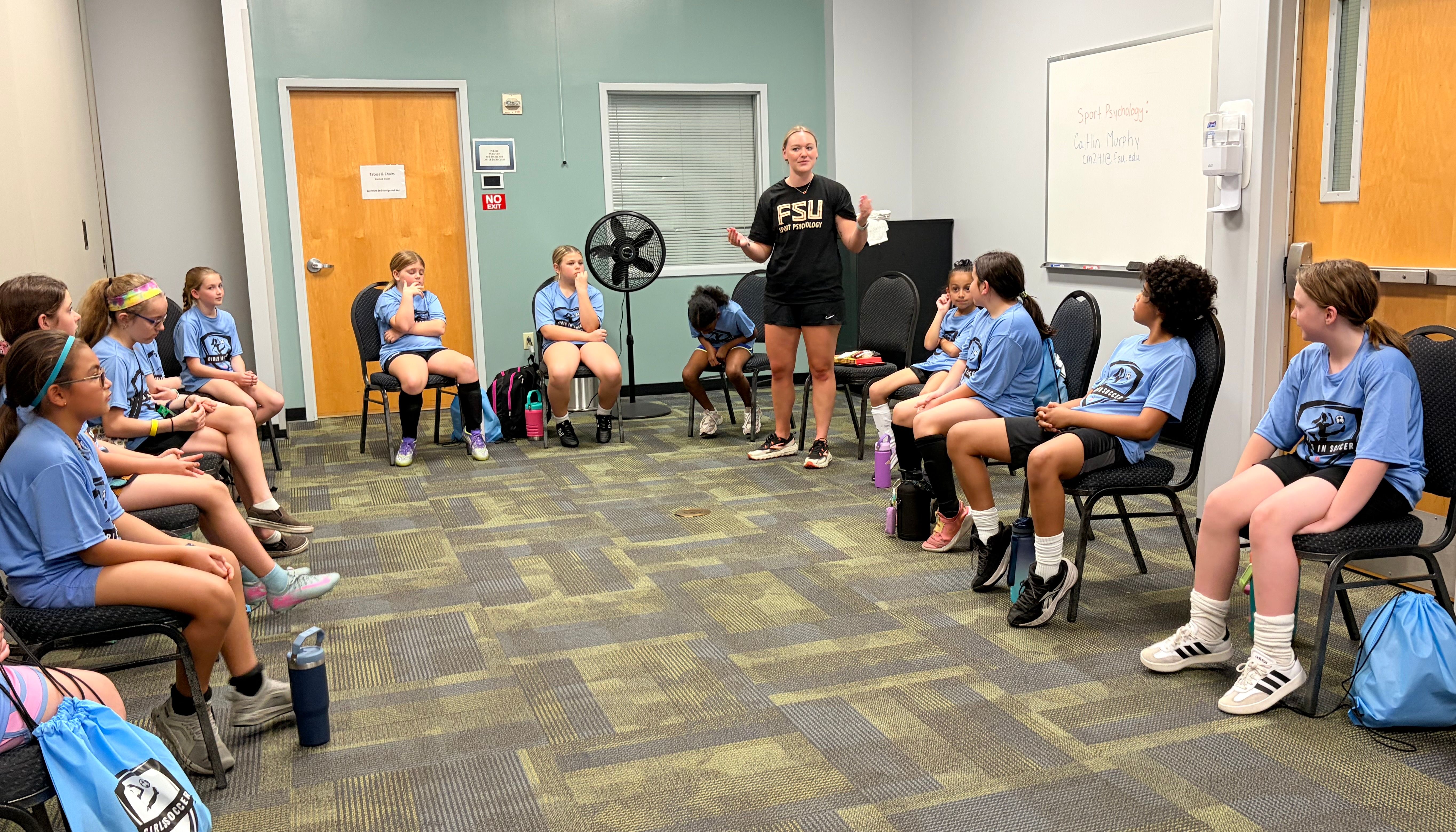 Girls in a circle listening to a coach during an education session.