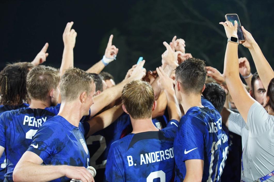 The Deaf MNT stands in a huddle with their arms up in blue jerseys
