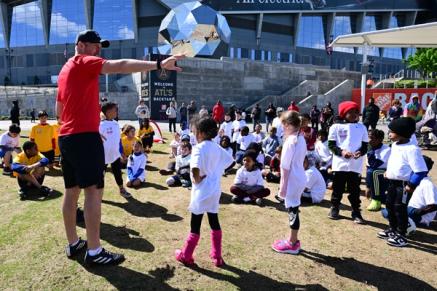A group of youth soccer players is instructed by a coach