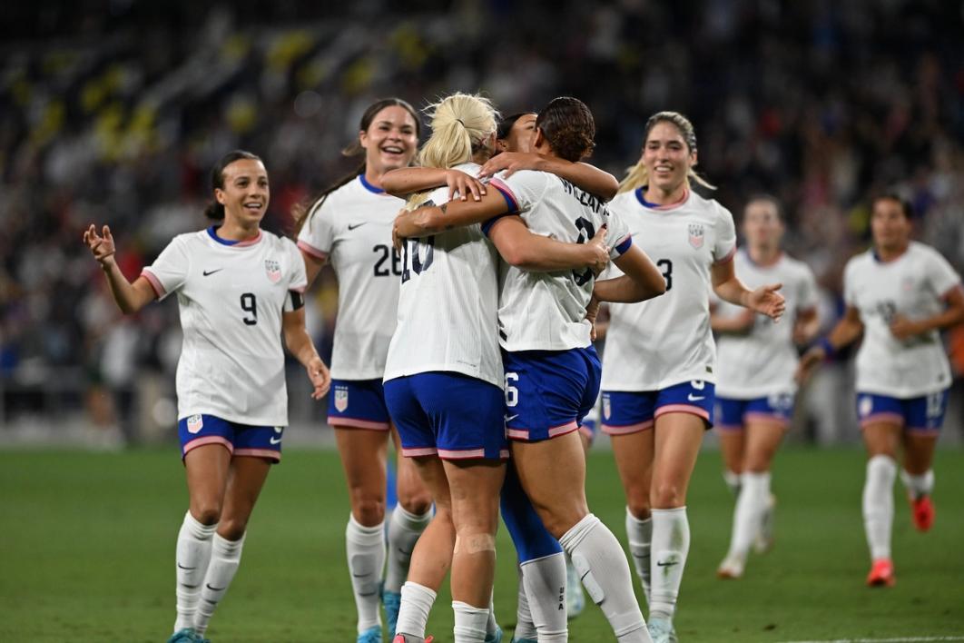 Members of the USWNT in white jerseys and blue shorts celebrate against Iceland