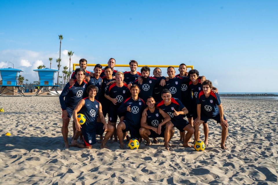 Members of the U.S. Men's Beach Soccer National Team post on a beach with soccer balls