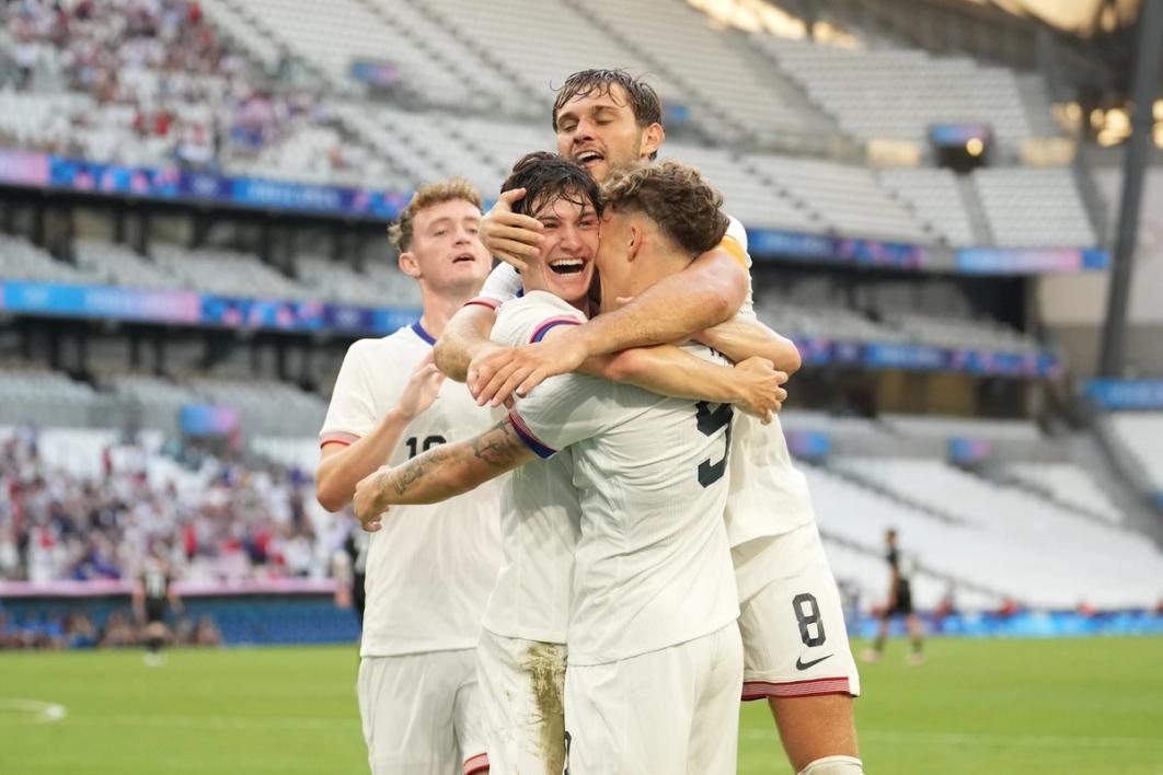 Four USA players embrace and celebrate a goal on the field during an Olympic match