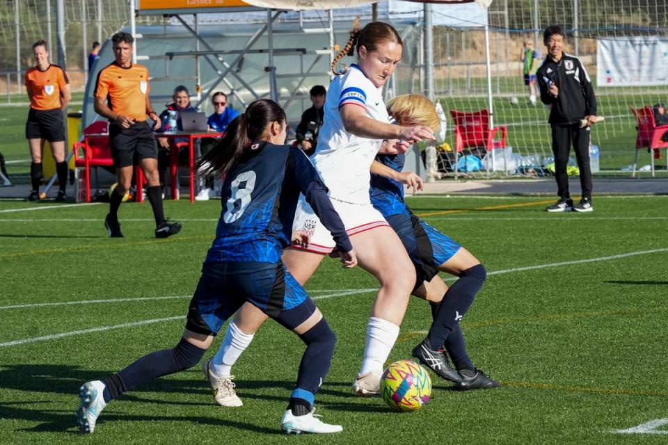 A US CP WNT player dribbles between two Japanese players during a match