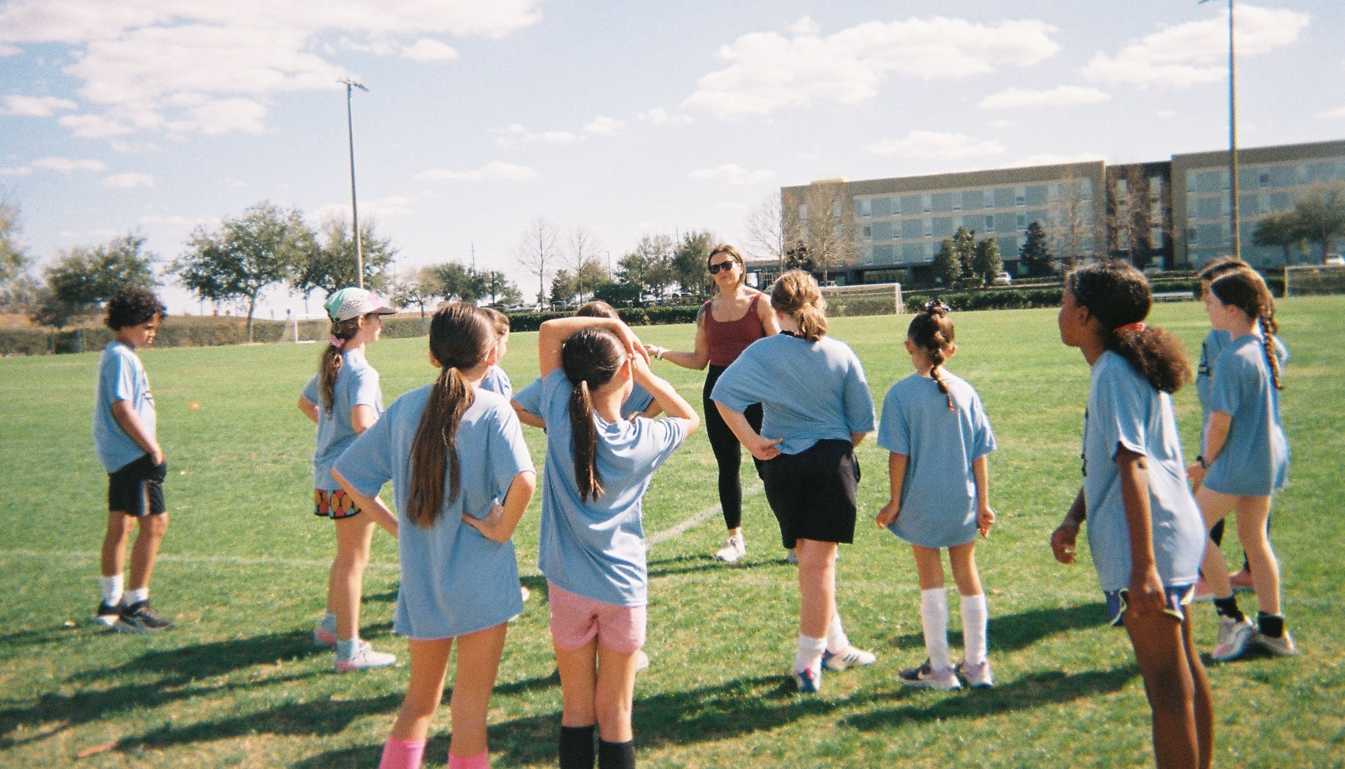 Girls in a circle listening to a coach during soccer practice.
