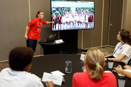 A presenter at the front of the room addresses a crowd