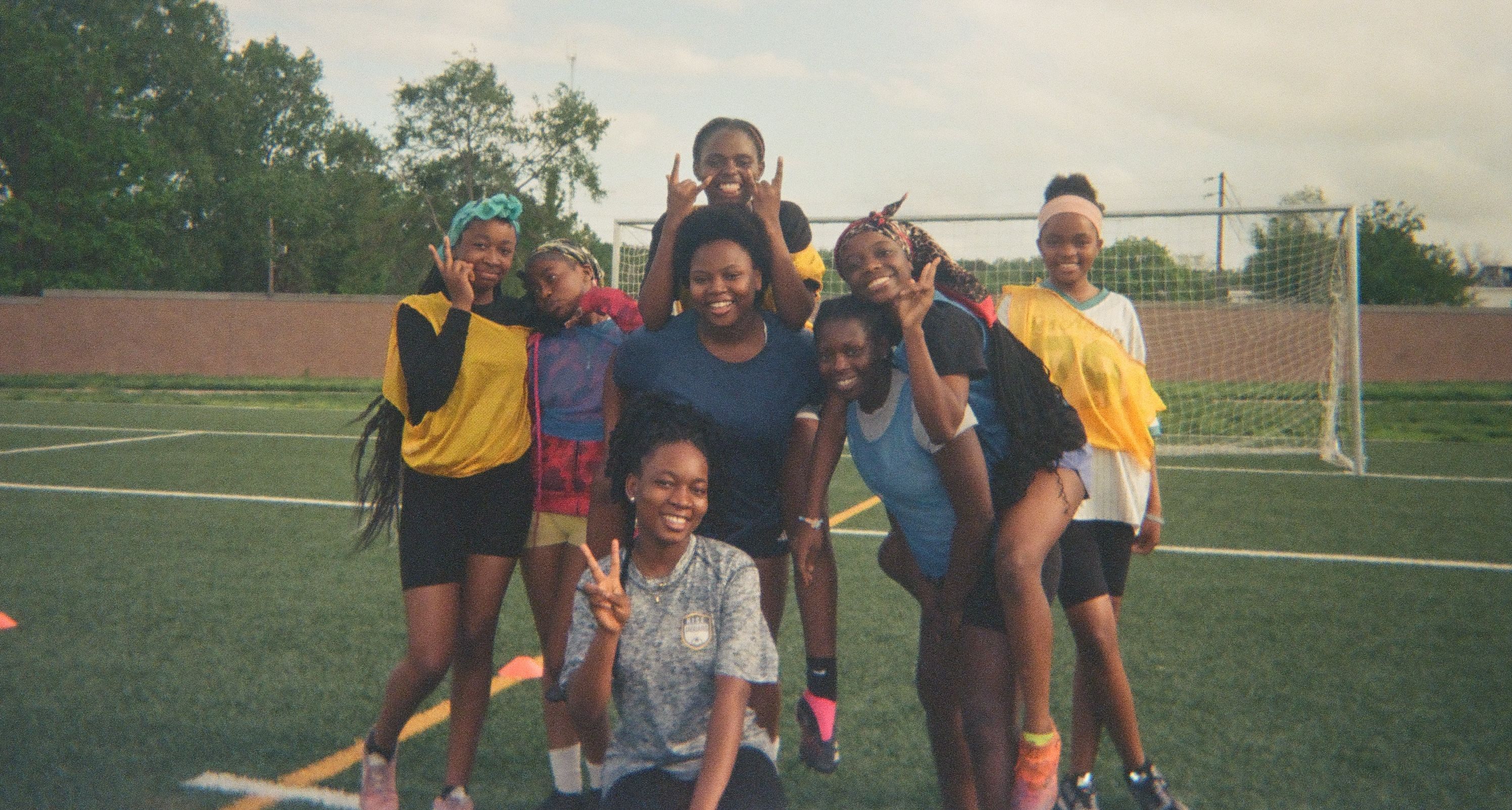 Group of children smiling and posing together on an outdoor soccer field.