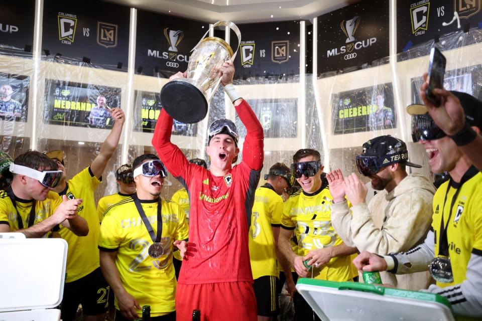 Schulte raising the cup in a locker room with players in goggles celebrating after a mls cup win