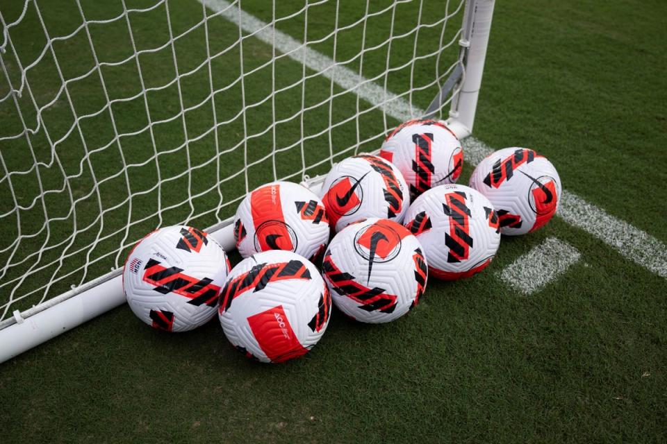 eight soccer balls on a field with a goal