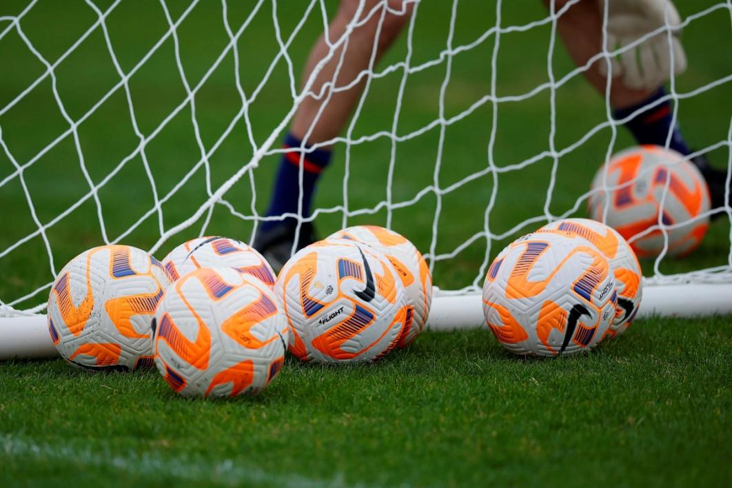 seven orange and white soccer balls in front of a net