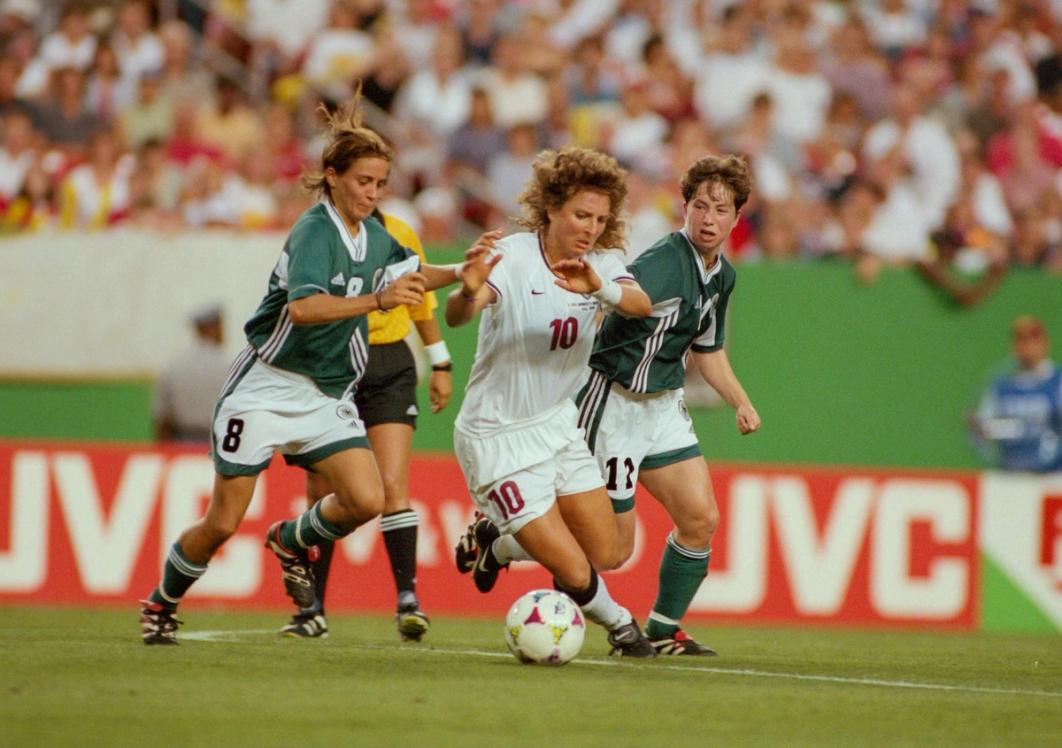 Michelle Akers dribbles the ball with two German defenders in pursuit