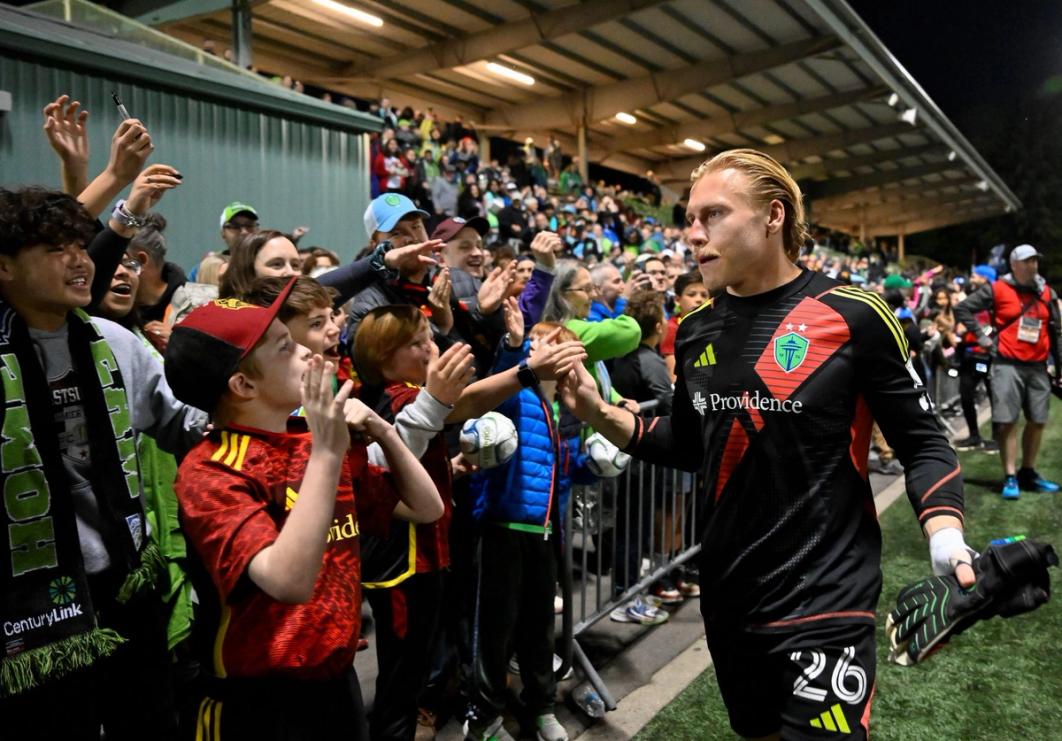 sounders goalkeeper in black and red jersey high fives kids in crowd after a match