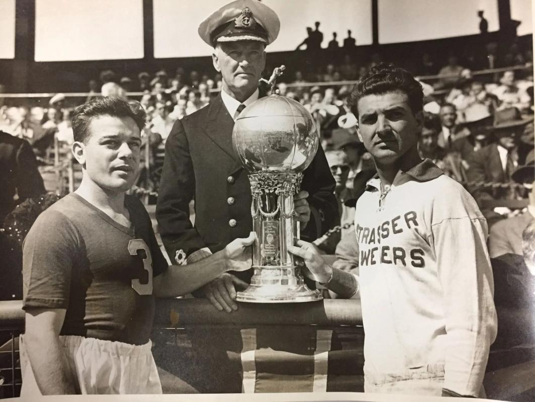 old time photo with two soccer players and a man in an old time military uniform touching a trophy