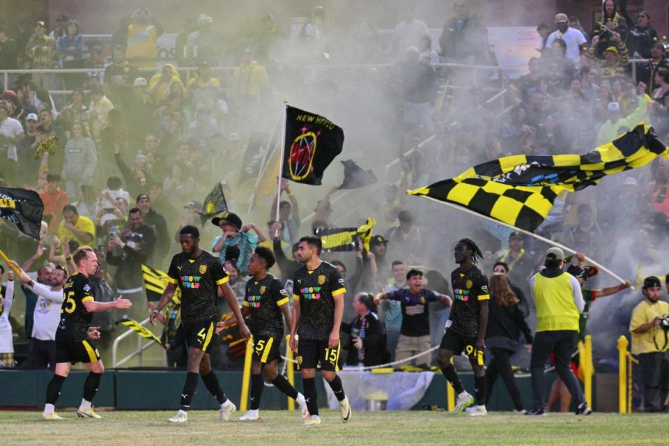 New Mexico United players walk onto the pitch with the crowd waving flags and smoke behind them