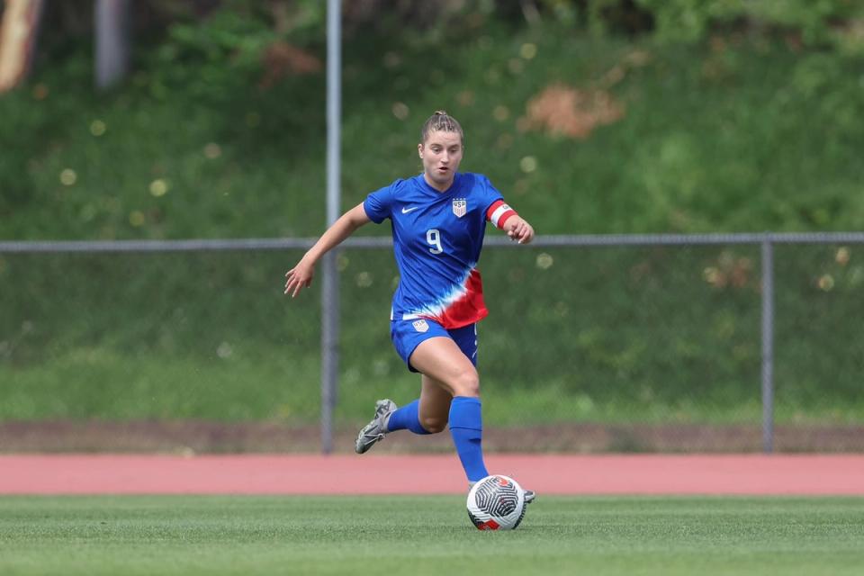 us no 9 in blue dribbles up the field with a ball