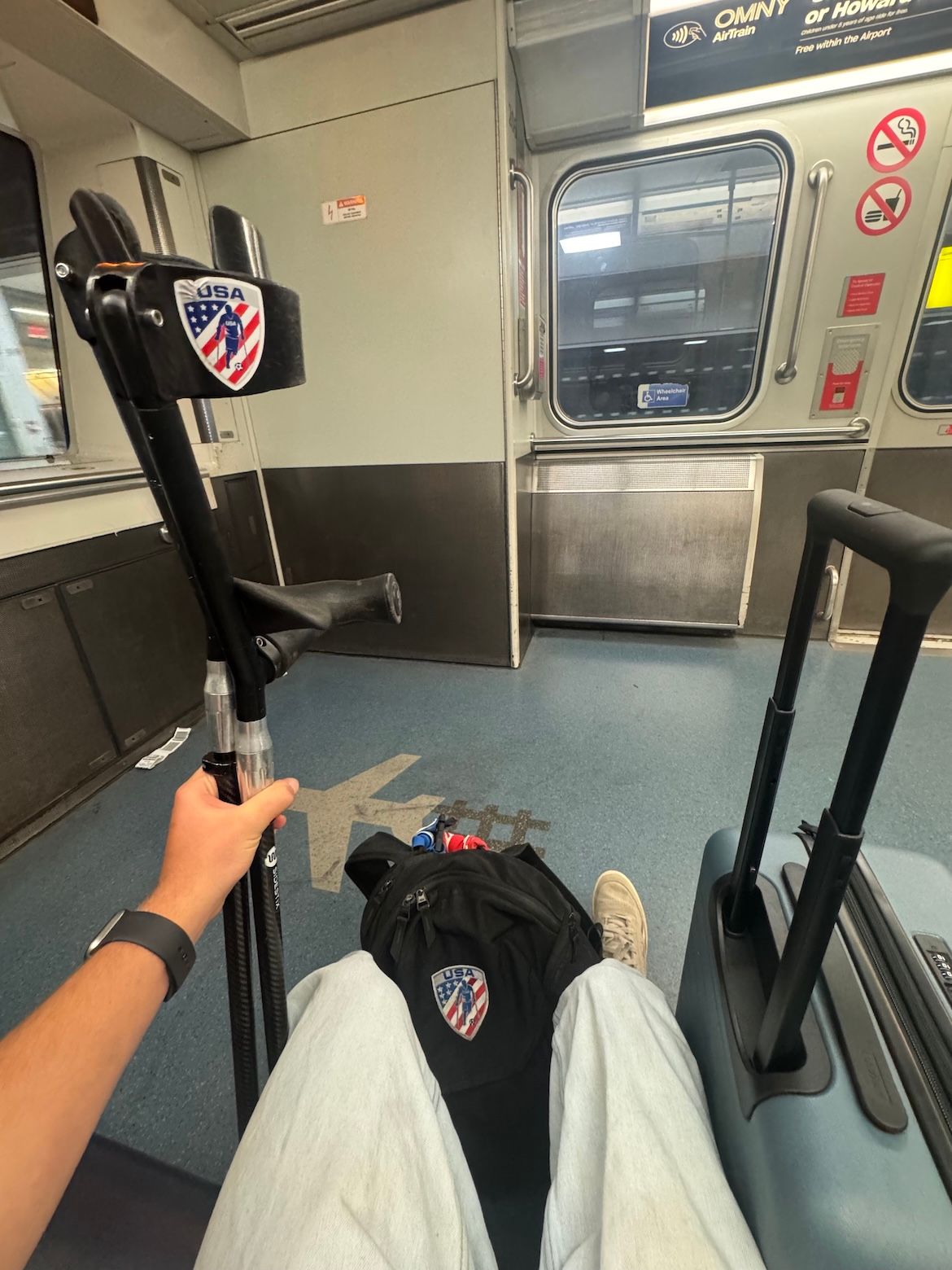 An amputee soccer player on a train with their crutches in one hand and bags around them