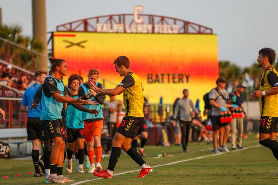 Charleston Battery players high fiving during on the sidelines of a match with a large video board in background