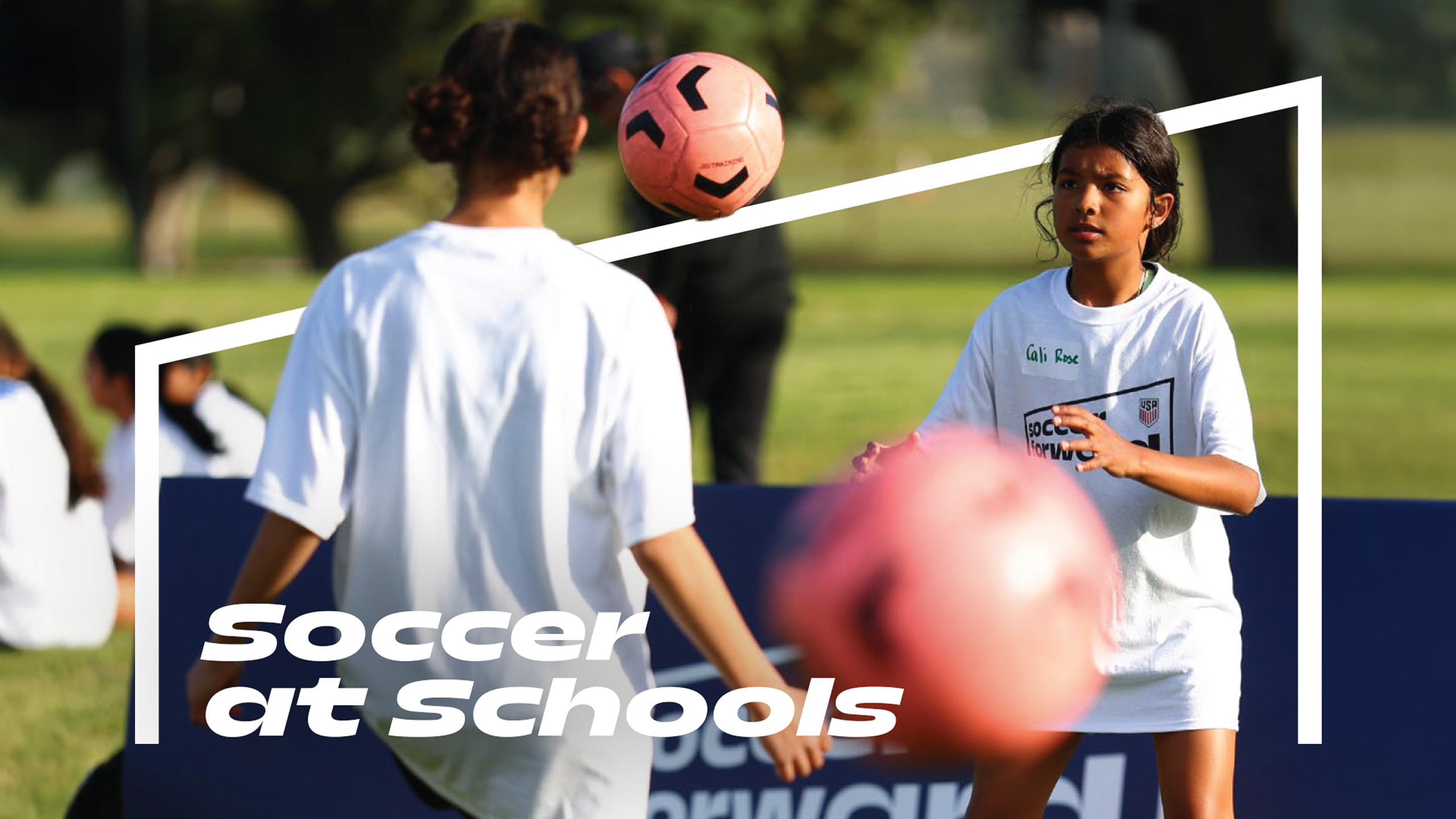 Two girls participate in a soccer activity at school, practicing ball control with a pink soccer ball on a grass field. Text on the image reads “Soccer at Schools.”