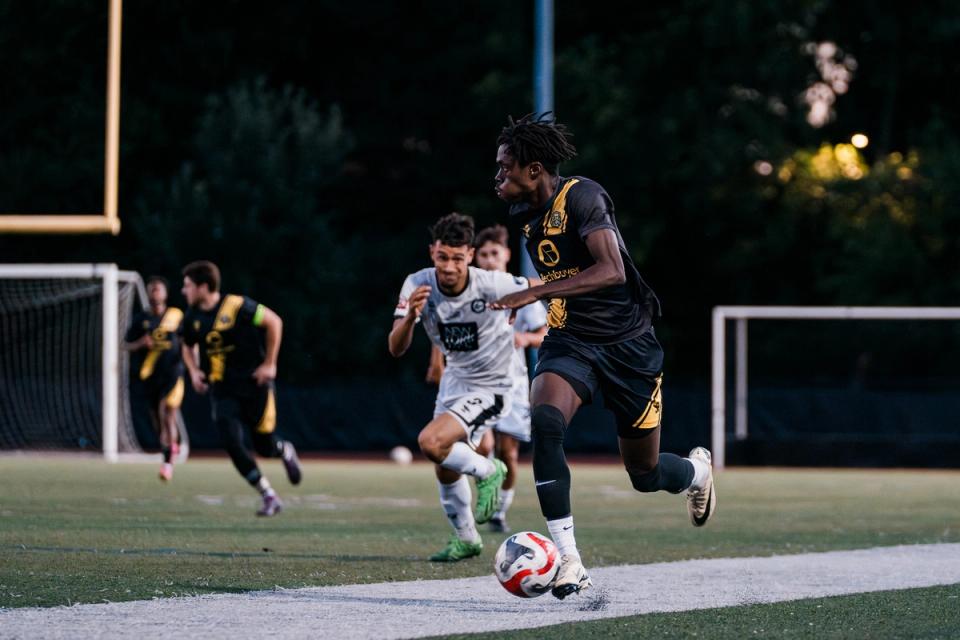 A player dribbles the ball down the pitch with a defender in pursuit