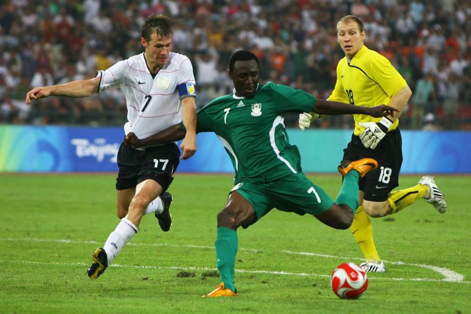 Chinedu Ogbuke Obasi of Nigeria kicks the ball away from Brian McBride and goalkeeper Brad Guzan
