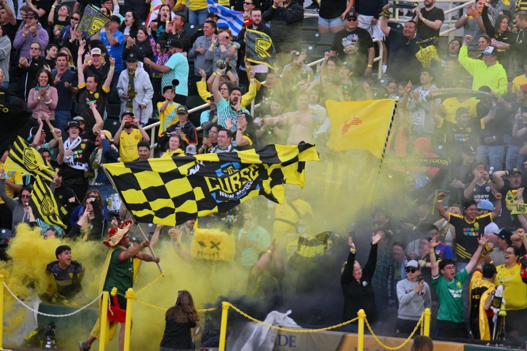 NMU Supporters in the crowd with yellow smoke and a flag that says The Curse