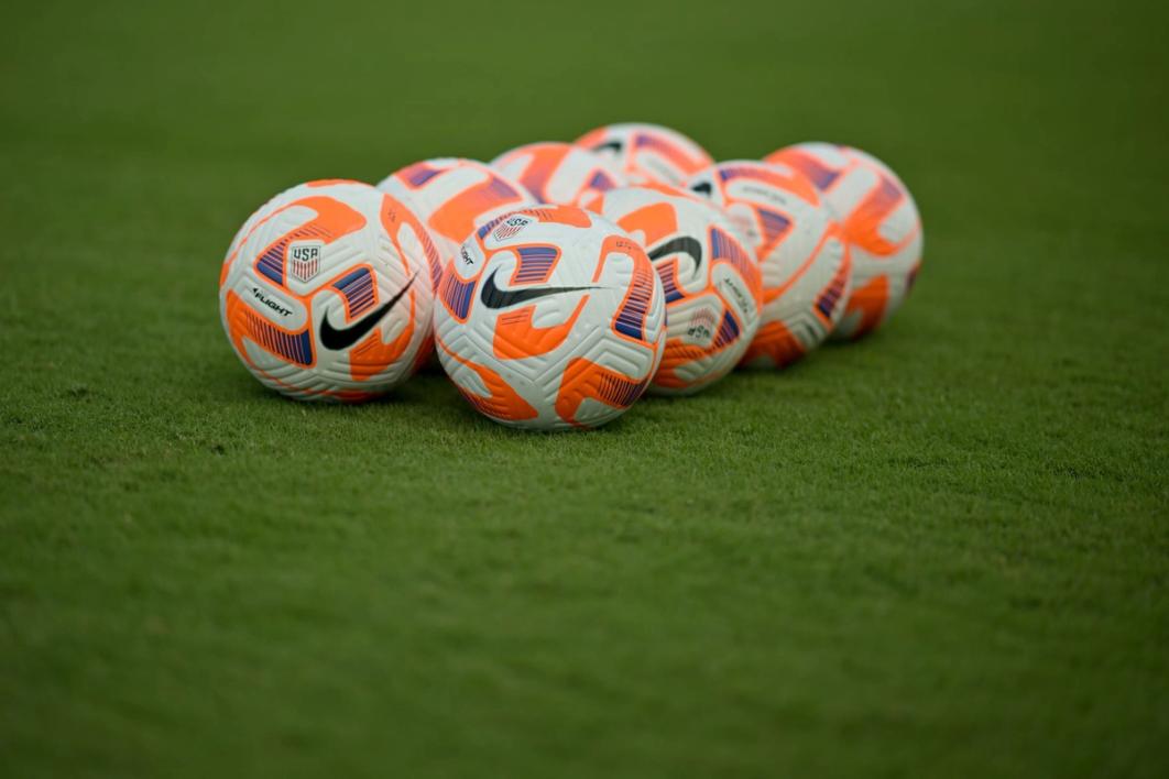 eight white and orange soccer balls on a field