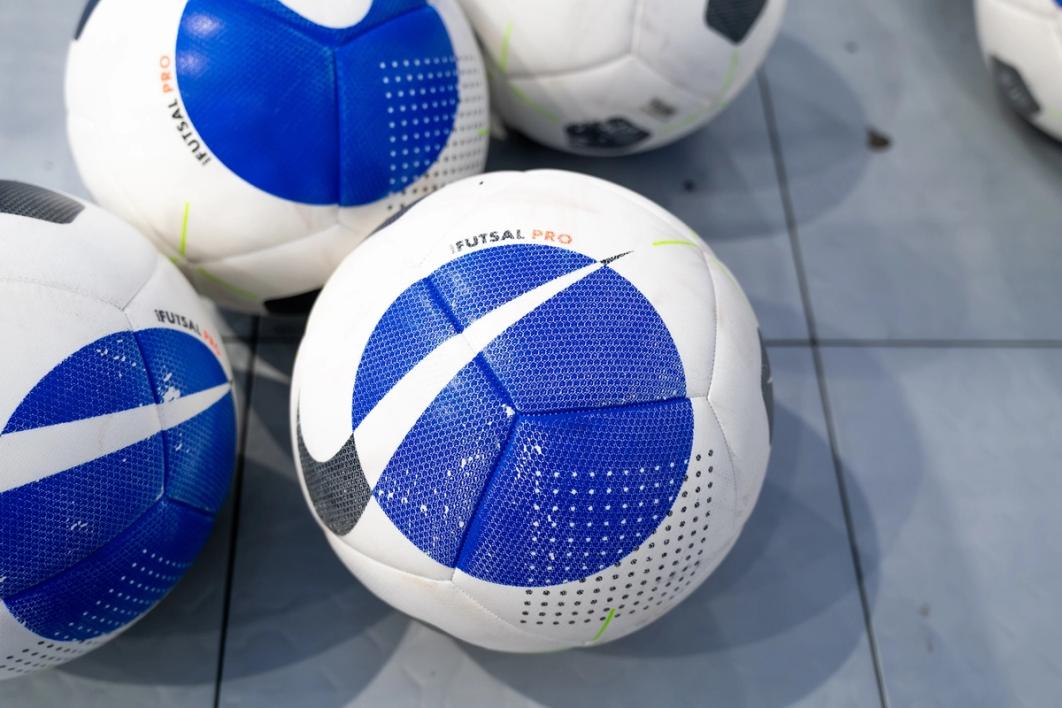 A photo of four soccer balls with a blue circle on them on a tiled floor