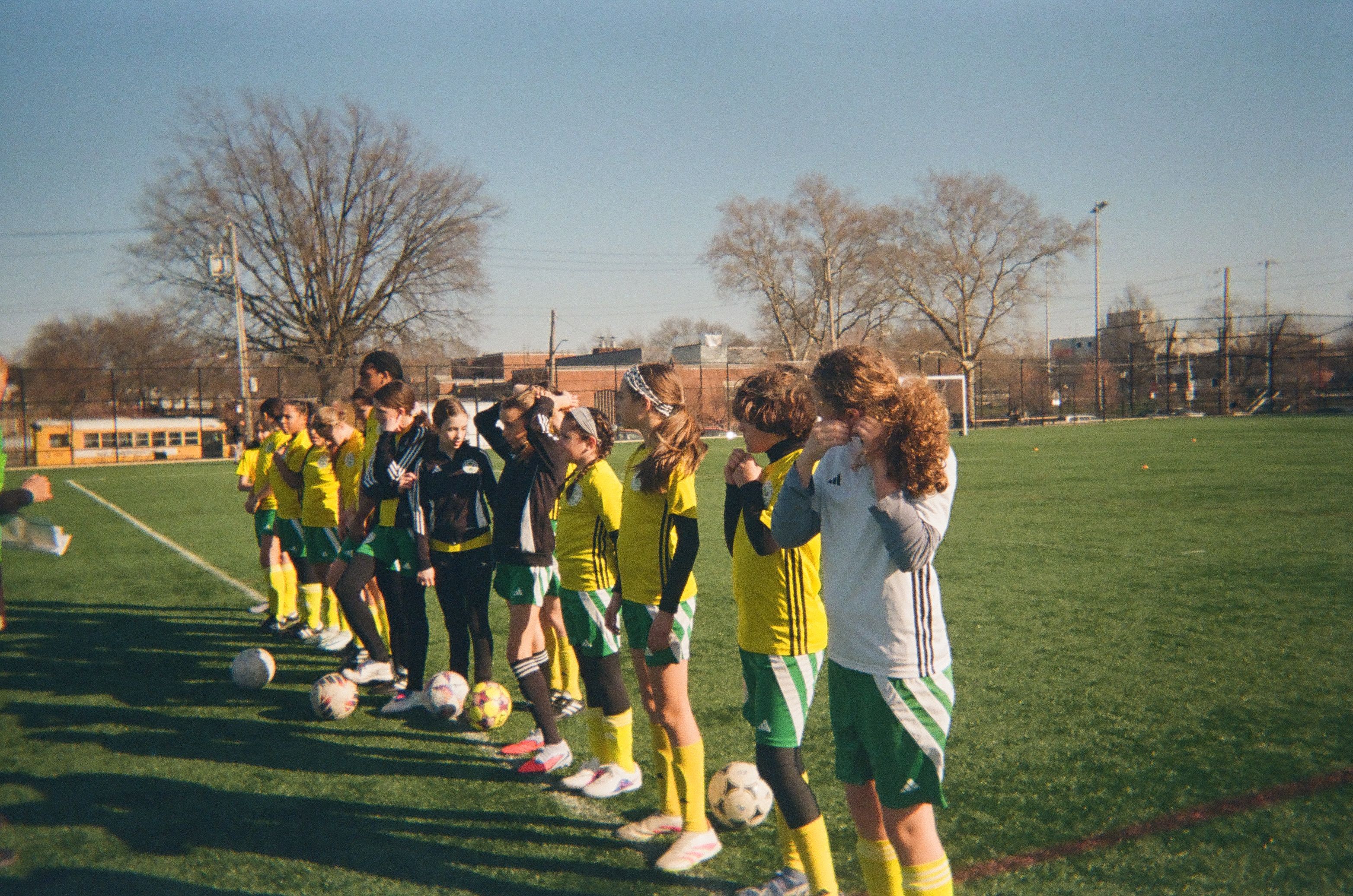 A group of girls standing on a sideline at a soccer event.