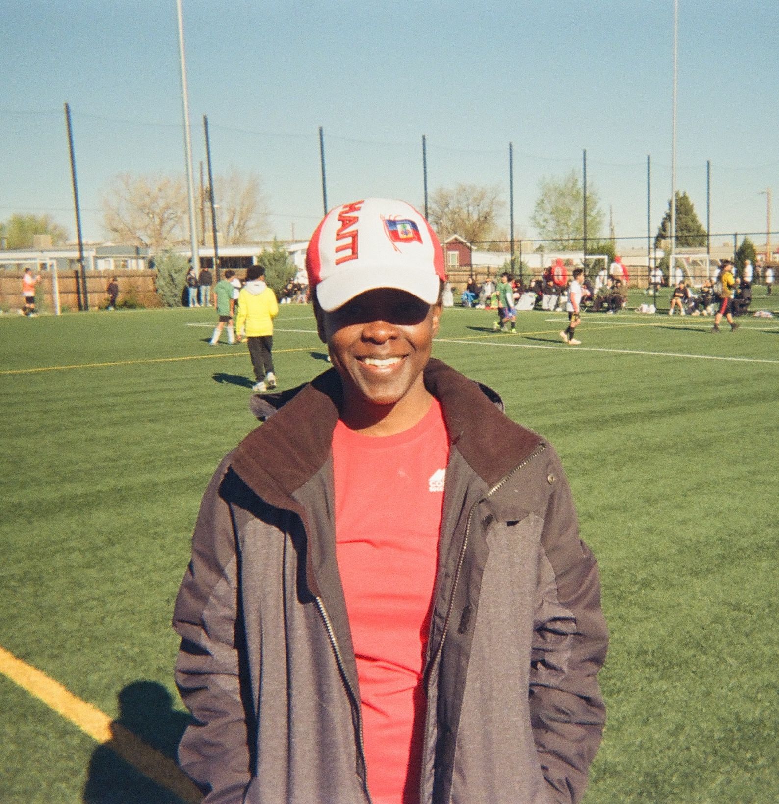 Person smiling on a soccer field wearing a Haiti cap during a community soccer event.