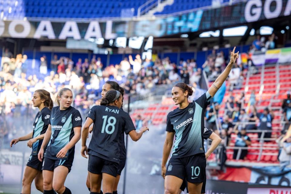 Lynn Williams waves to the crowd during a Gotham FC match with teammates to her left and crowd in the background