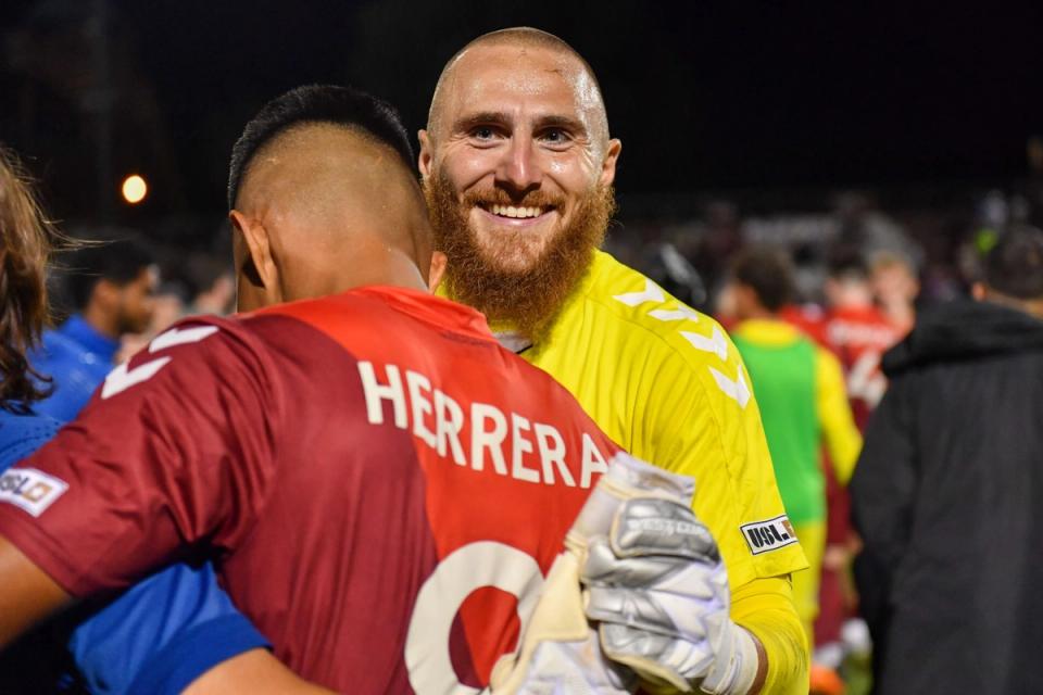 A player in a yellow goalkeeper kit embraces a player with a red kit and last name Herrera after an Open Cup match