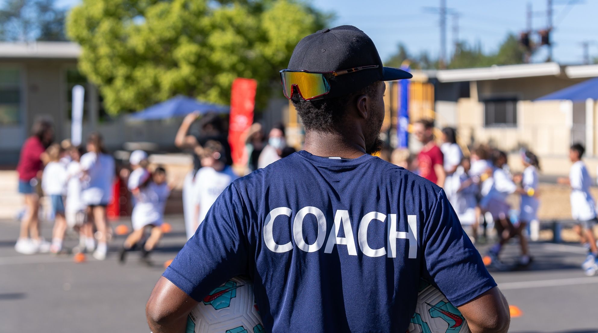 Coach overseeing a group of children participating in a soccer activity at a school playground.