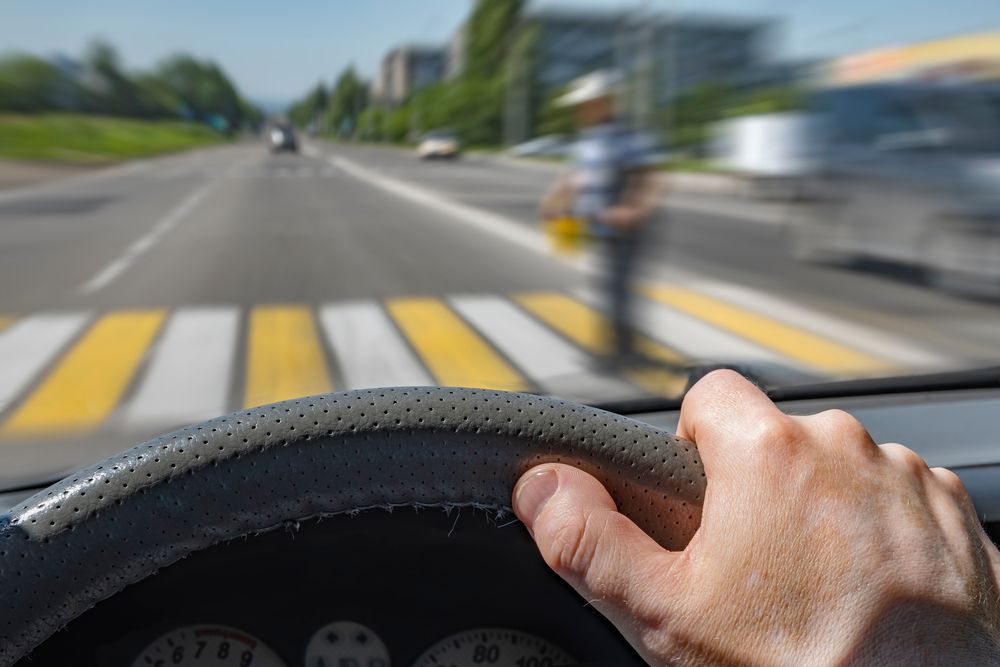 Driver’s view of a crosswalk with a blurred pedestrian crossing, illustrating how pedestrian accidents can happen in Brooklyn traffic.