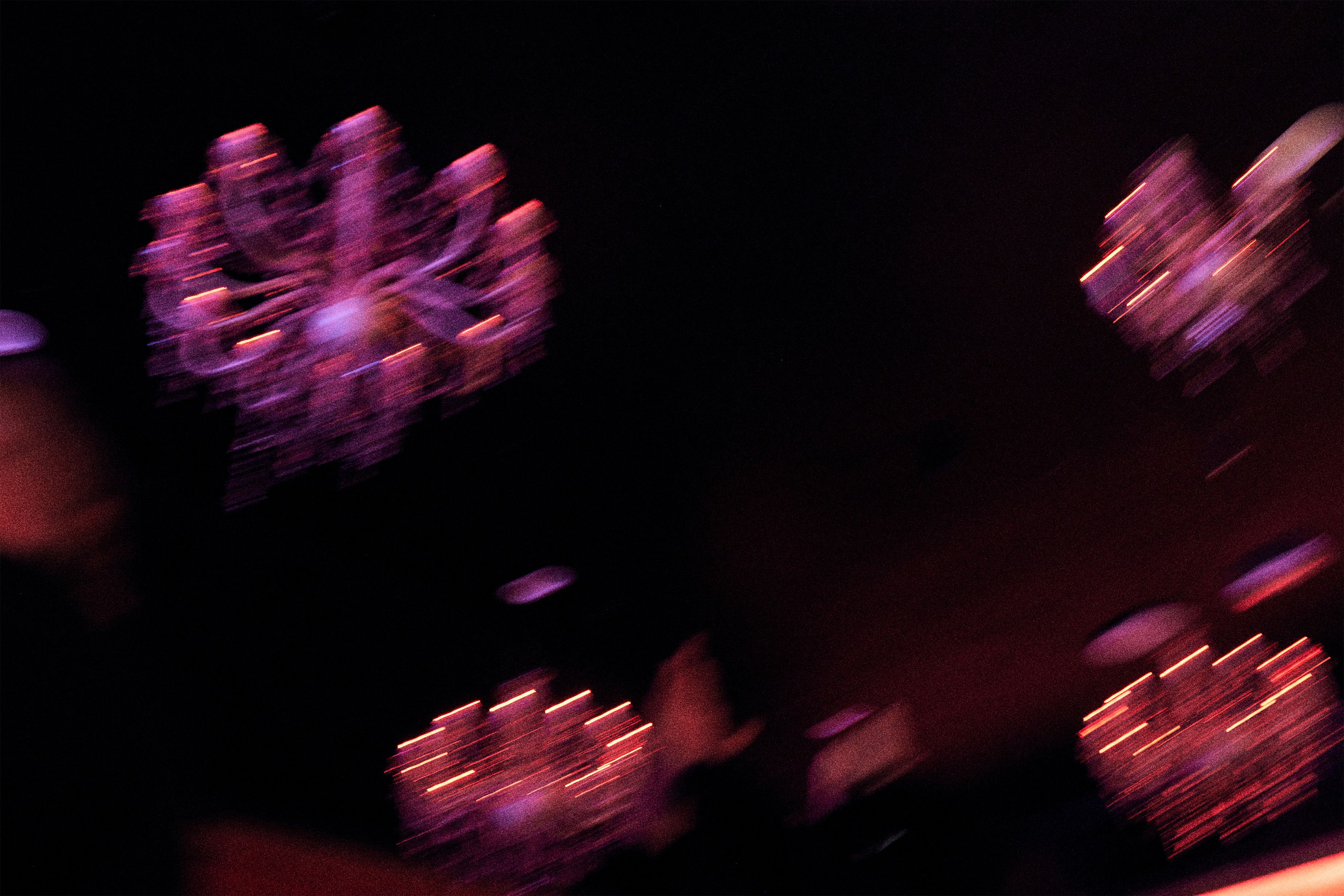 A blurry, low-light shot features glowing purple and pink chandeliers hanging in a dark space. The motion blur creates streaks of light that suggest a dynamic, nocturnal atmosphere.