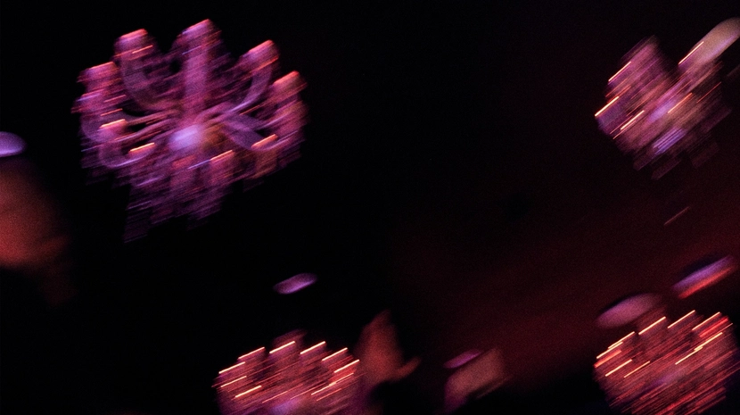 A blurry, low-light shot features glowing purple and pink chandeliers hanging in a dark space. The motion blur creates streaks of light that suggest a dynamic, nocturnal atmosphere.