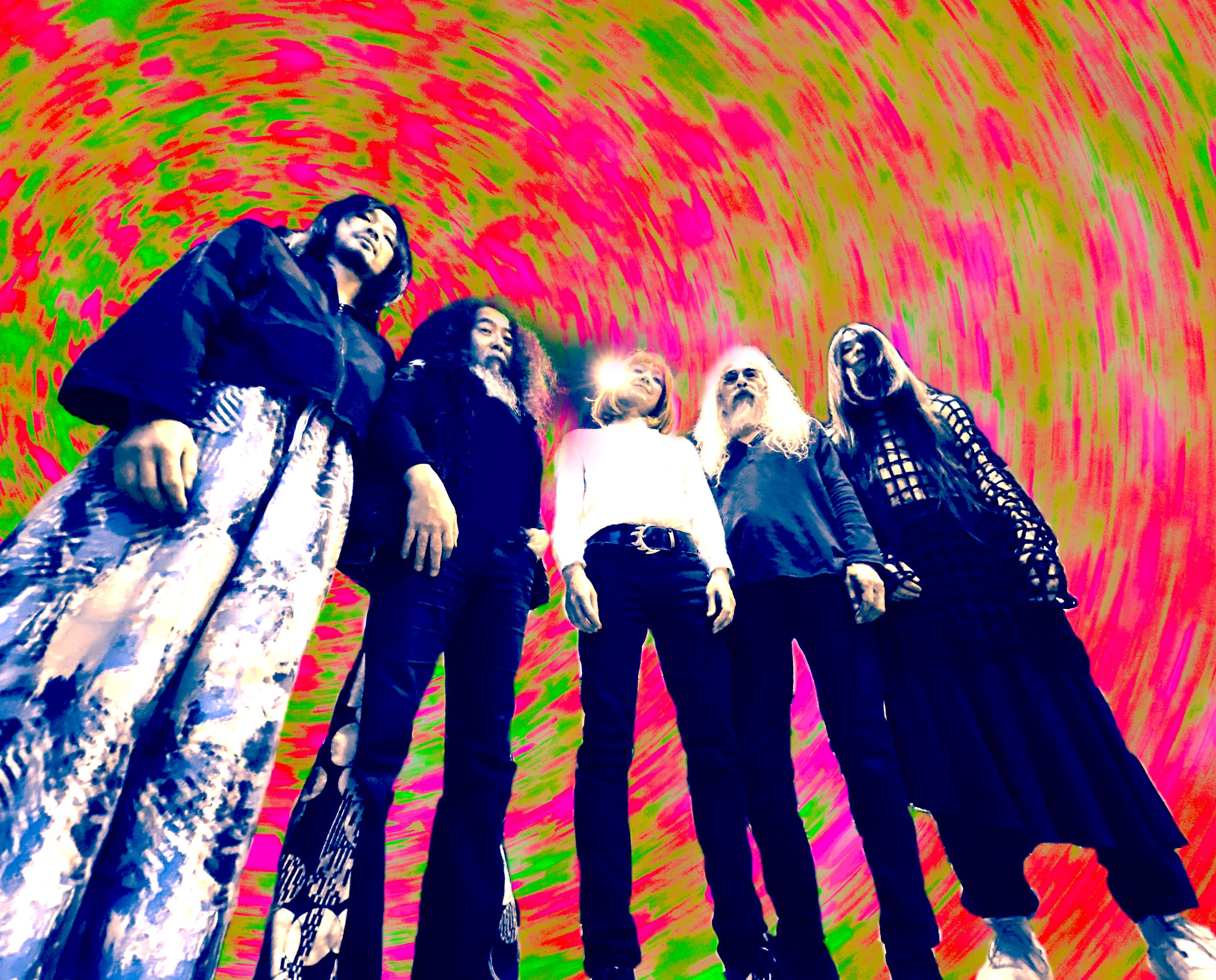 A low-angle shot of five band members standing against a vibrant, swirling psychedelic backdrop of hot pink and lime green. The figures are captured in a stylised, high-contrast edit that emphasises their long hair and eclectic clothing.