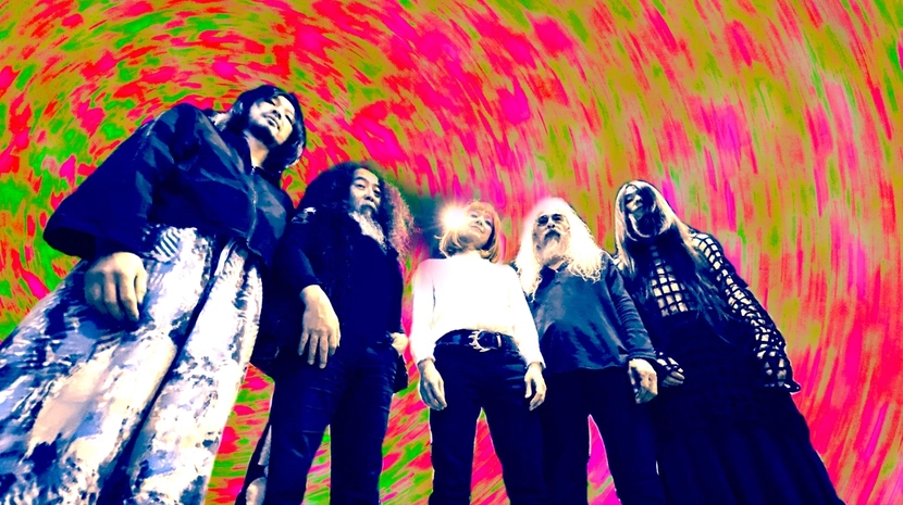 A low-angle shot of five band members standing against a vibrant, swirling psychedelic backdrop of hot pink and lime green. The figures are captured in a stylised, high-contrast edit that emphasises their long hair and eclectic clothing.