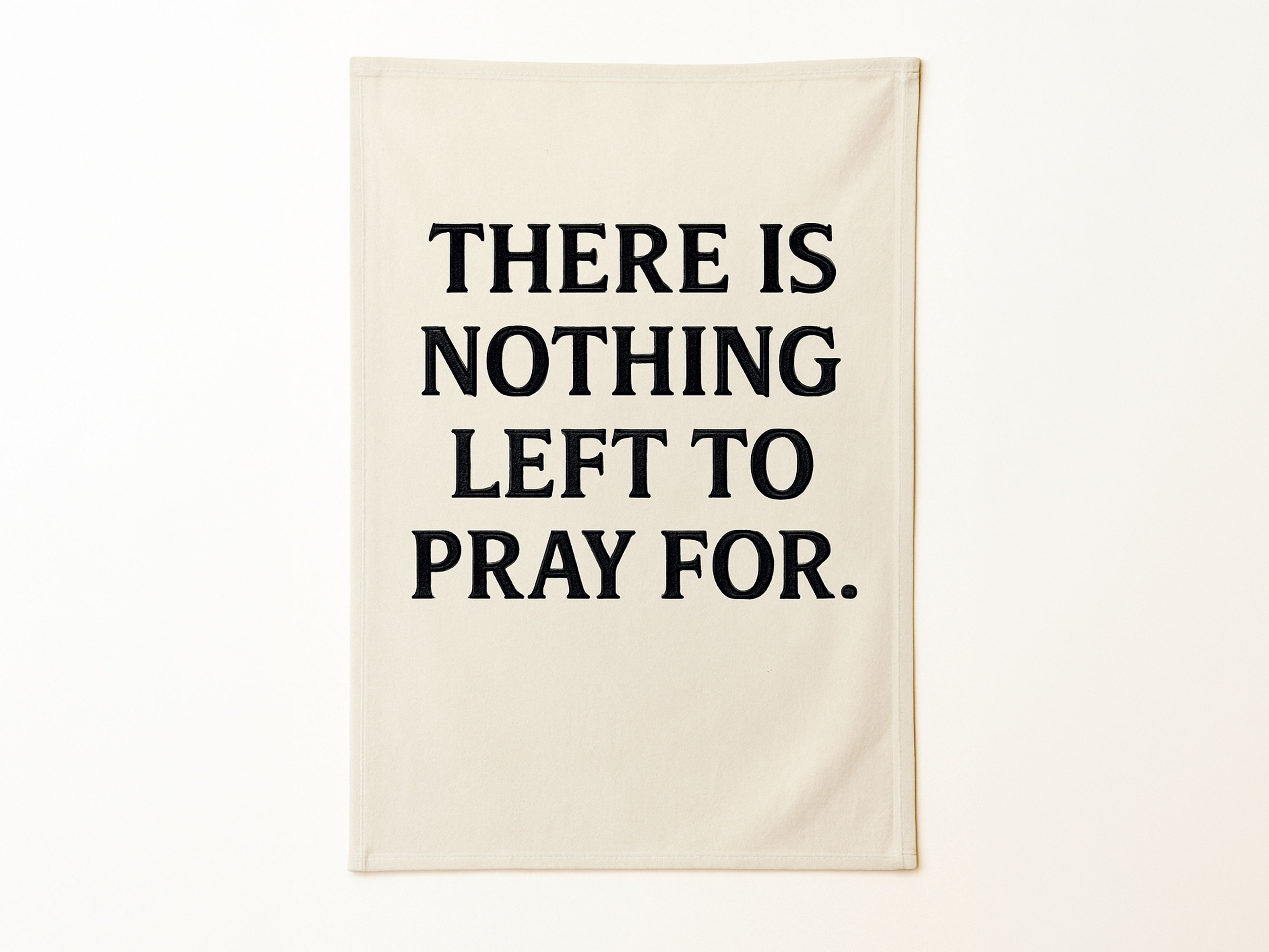A minimalist textile art piece featuring a cream-colored fabric banner with the words "THERE IS NOTHING LEFT TO PRAY FOR." embroidered in bold, black capital letters. The banner hangs flat against a plain, off-white wall.