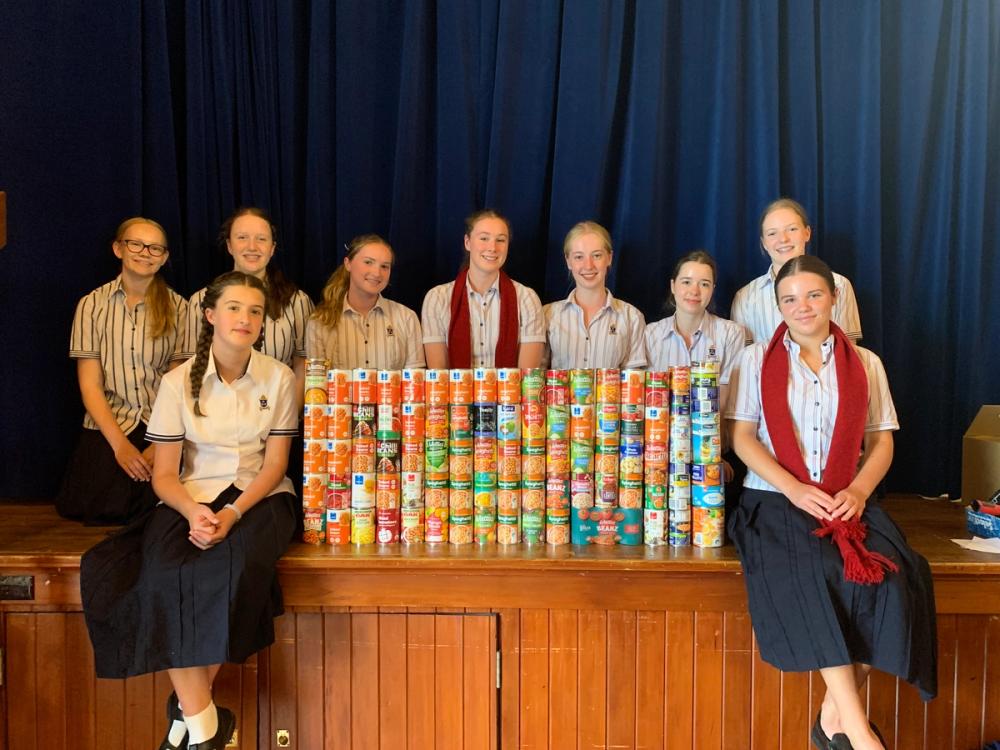 a group of students sitting on a stage with a stack of tinned food
