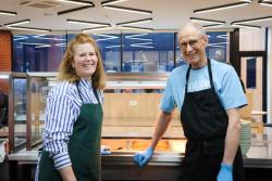 a man and a woman wearing aprons are standing next to each other in a kitchen .