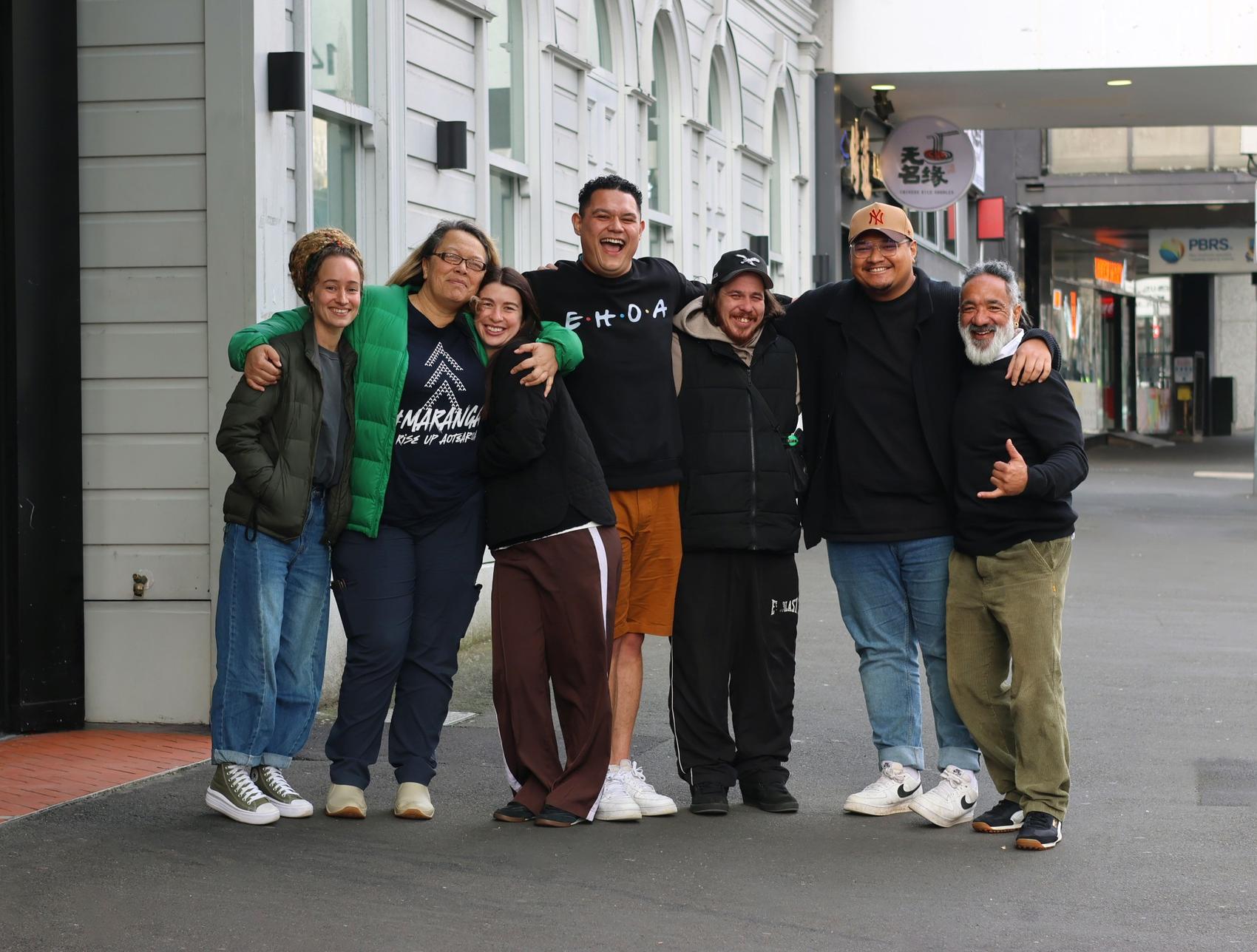 a group of people are posing for a picture on the sidewalk in front of a building .