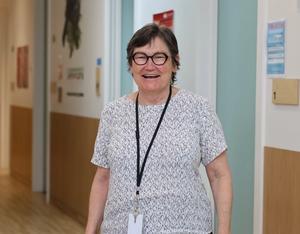 a woman wearing glasses and a lanyard is standing in a hallway and smiling .