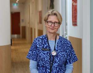 a woman in a blue scrub top with a stethoscope around her neck is standing in a hallway .